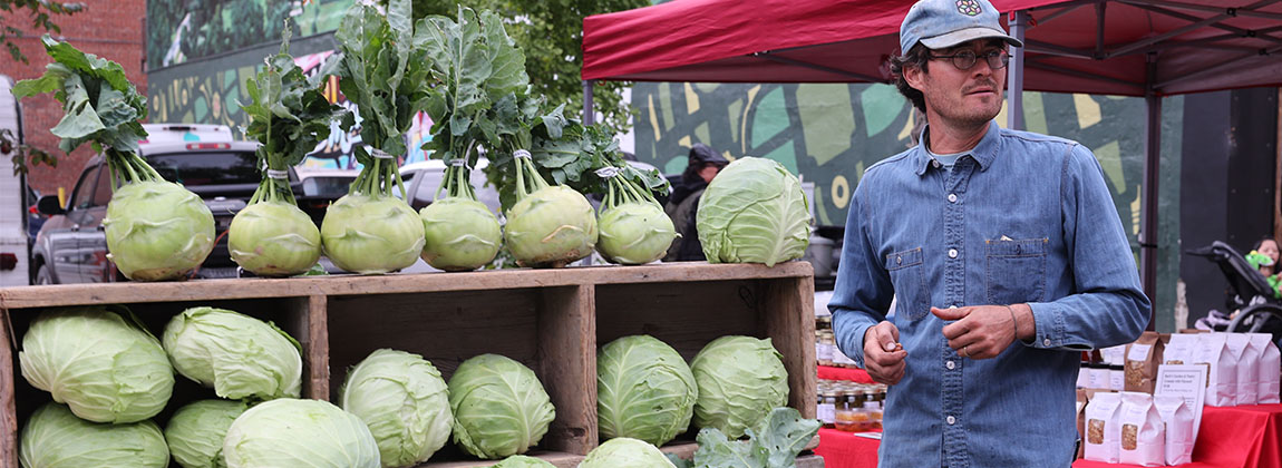 Fall produce displayed on a table with a vendor standing next to it.